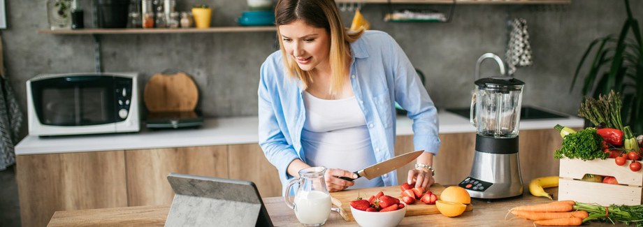 Young pregnant woman enjoying making healthy food in the kitchen